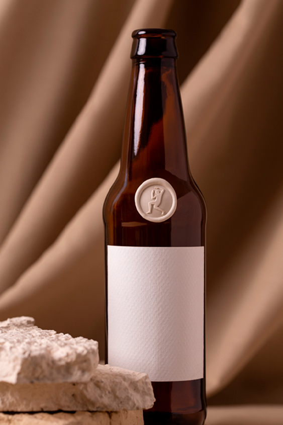Brown beer bottle with a champagne medallion, the design of the medallion is the silhouette of a man, it has a white label without text.