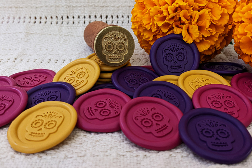 Purple, yellow and magenta wax stickers with catrina design, sealing wax seal with catrinas design too, and cempasúchil flowers