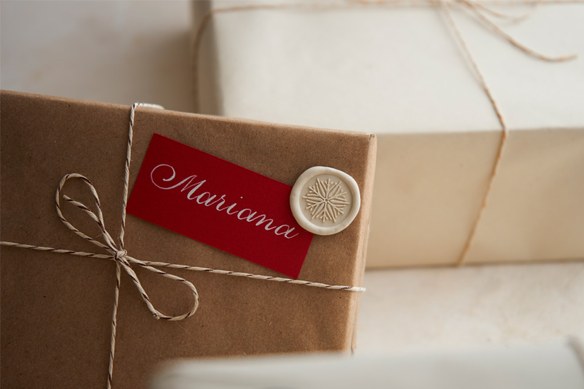 Gift box with a red card that has the name Mariana written in calligraphy, and an ivory sealing wax medallion with a snowflake design