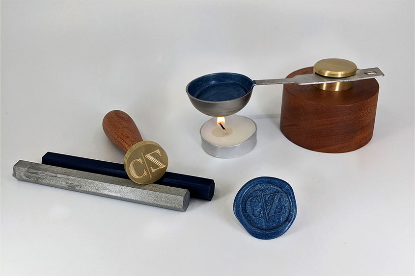 Mini melting base with fused metallic blue sealing wax, mix of silver and navy blue sealing wax bars, and a seal with CZ initials