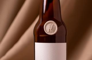 Brown beer bottle with a champagne medallion, the design of the medallion is the silhouette of a man, it has a white label without text.
