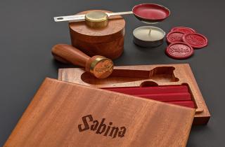 Wooden case from a sealing wax set that has engraved the name Sabrina on top. Inside the case there are 3 read sealing wax bars, a wooden handle and a