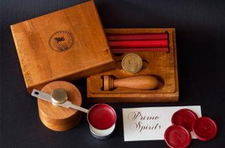 Wooden case from a sealing wax set that has a flag engraving on top and a melter with red sealing wax. Inside the case there are 3 sealing wax bars, a
