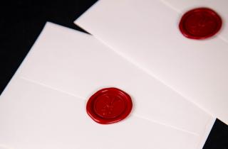 Sealed white envelope with the line wax seal greek flower in color red