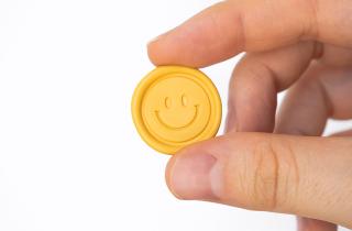 Yellow sealing wax sticker with happy face design, holded by a hand in a white background