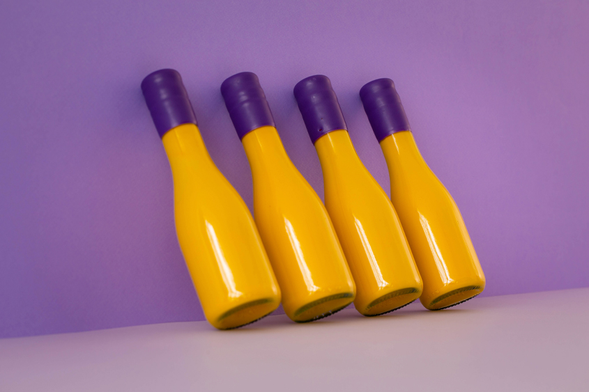 4 yellow bottles with purple sealing wax on the neck of the bottle and at the background is a dark purple wall and light purple floor