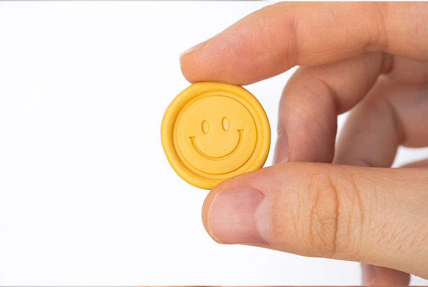 Yellow sealing wax sticker with happy face design, holded by a hand in a white background